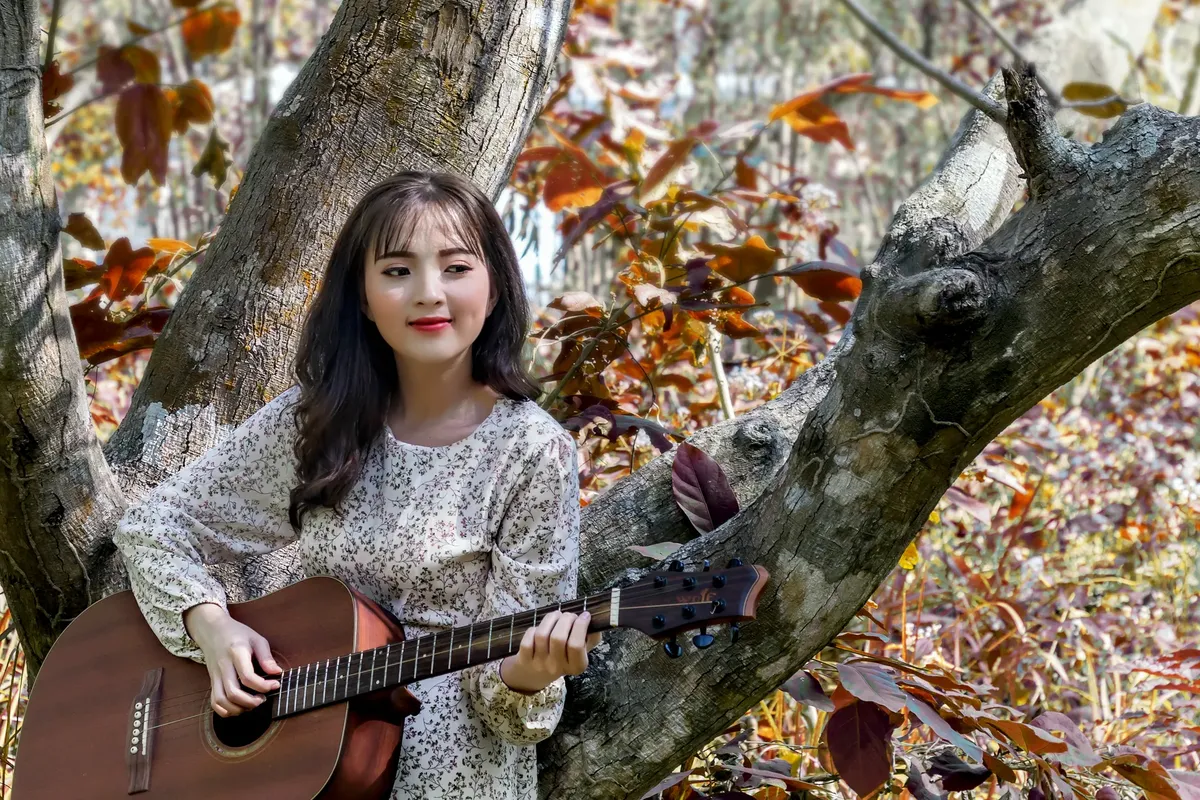 Young woman playing acoustic guitar in a serene outdoor setting in An Giang, Vietnam.