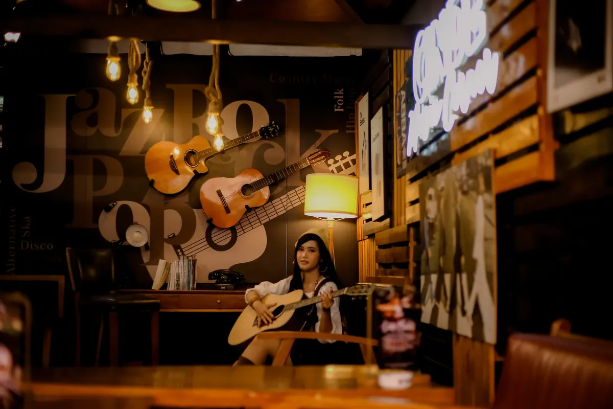 Warm music-themed café interior featuring a woman playing guitar, illuminated by soft lighting.
