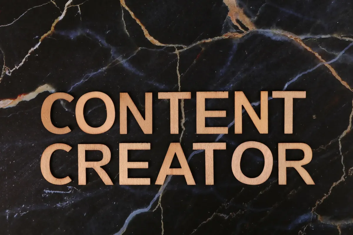 어두운 마르블 배경 위에 나무로 만든 글자로 'CONTENT CREATOR'가 새겨져 있습니다.