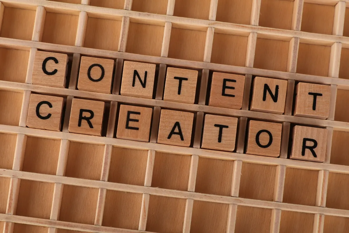 그리드 배경 위에 나무 블록 글자로 'Content Creator'가 새겨져 있습니다. 디지털 마케팅 테마에 이상적인 이미지입니다.