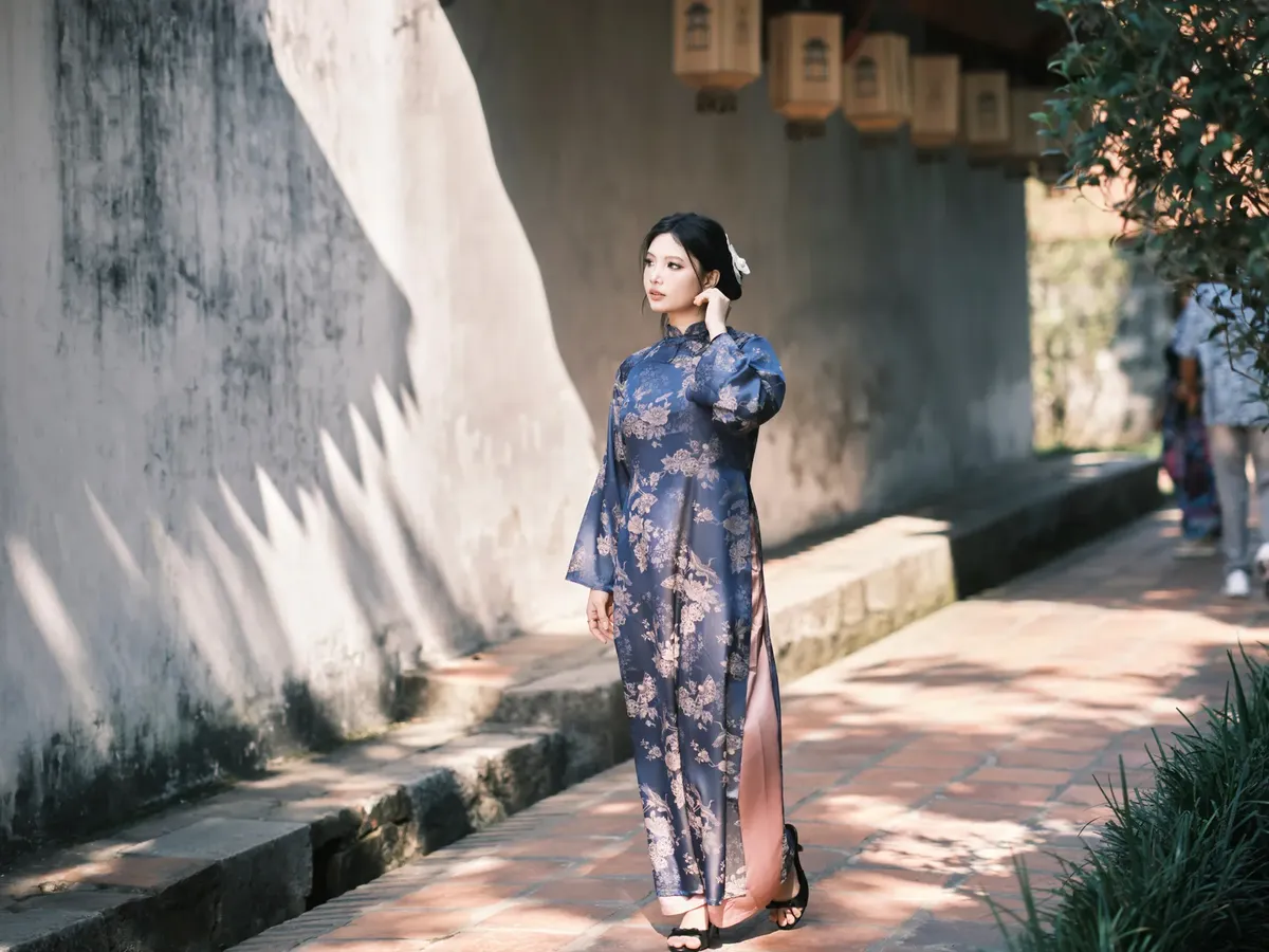 花模様のアオダイを着た女性が、陽光に照らされた屋外で歩く様子、伝統的なファッションを紹介する